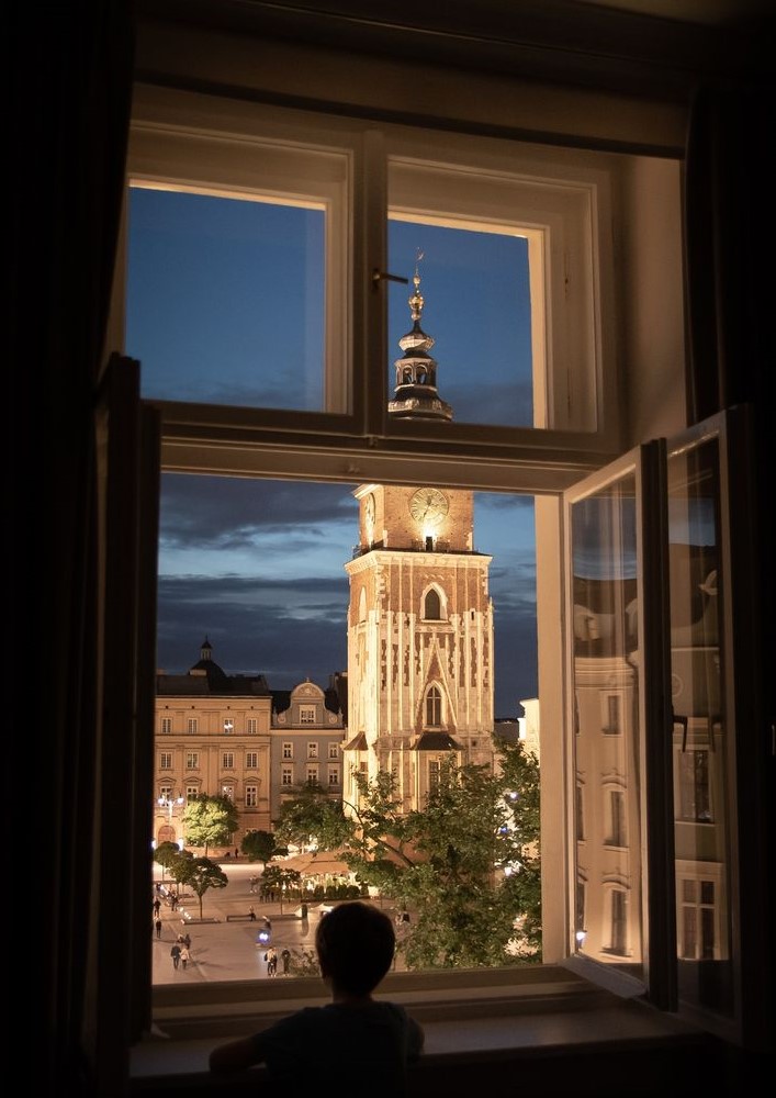 Kraków Town Hall Tower illuminated at dusk seen through an open window